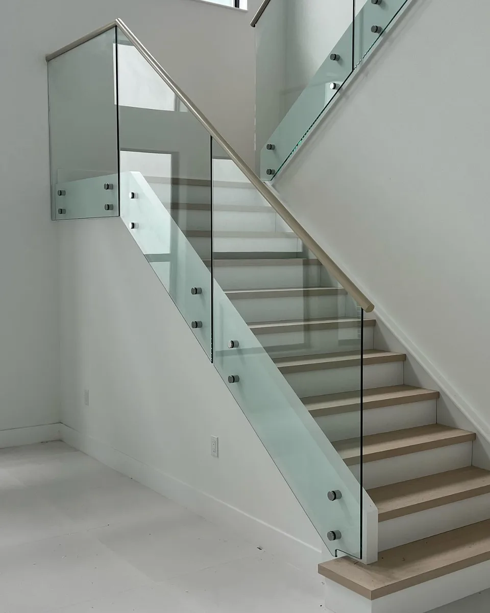Baranda de vidrio referencial con pasamanos metálico en escalera minimalista blanca
