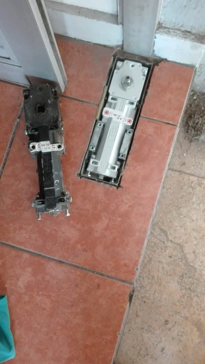 Quicio de piso instalado junto a mecanismo anterior retirado de una puerta comercial
