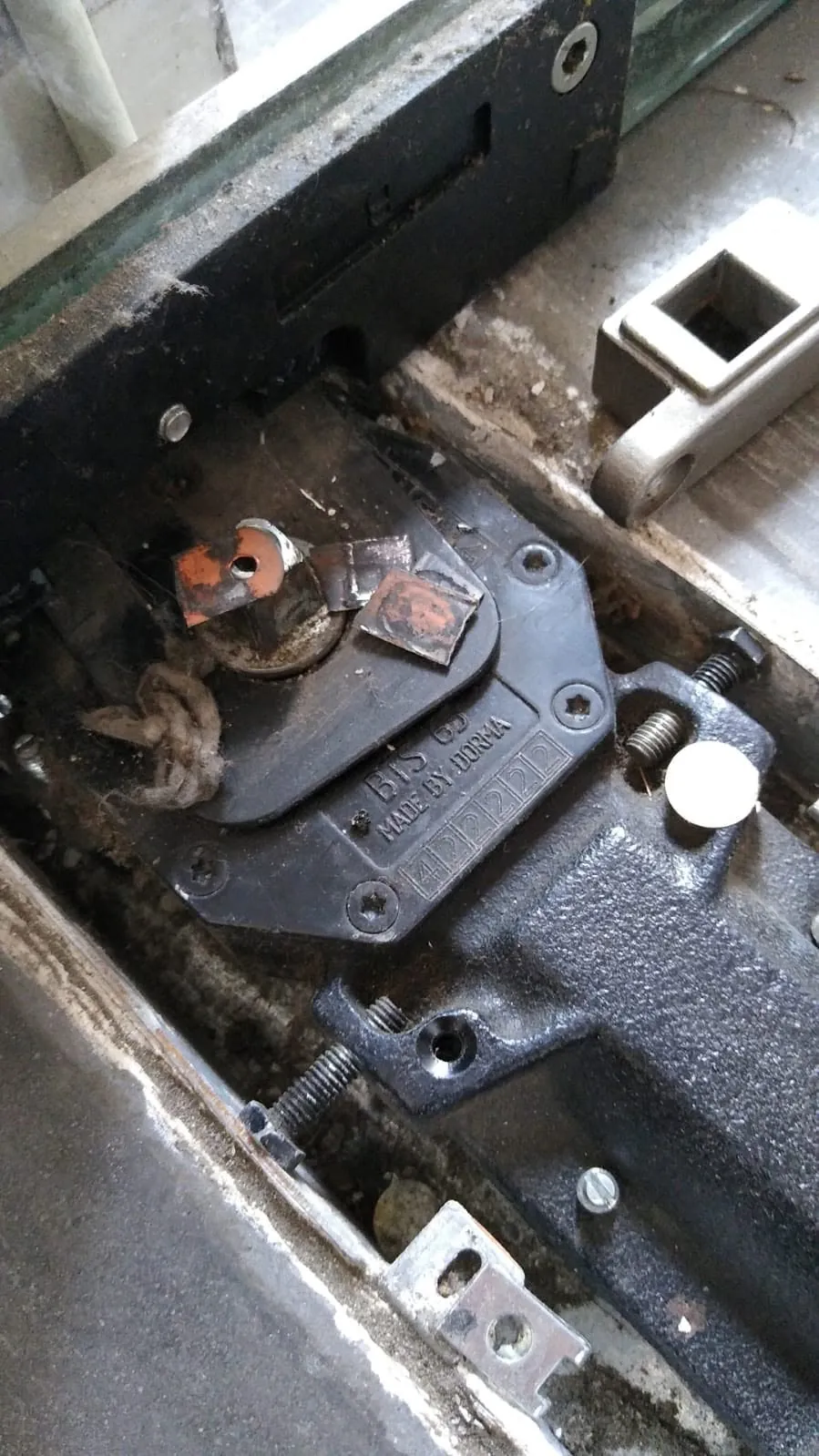Detalle real de mecanismo hidráulico antiguo de puerta con suciedad y corrosión en sus piezas