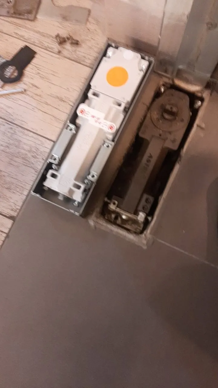 Mecanismo antiguo y quicio hidráulico nuevo dispuestos junto a una puerta de acceso